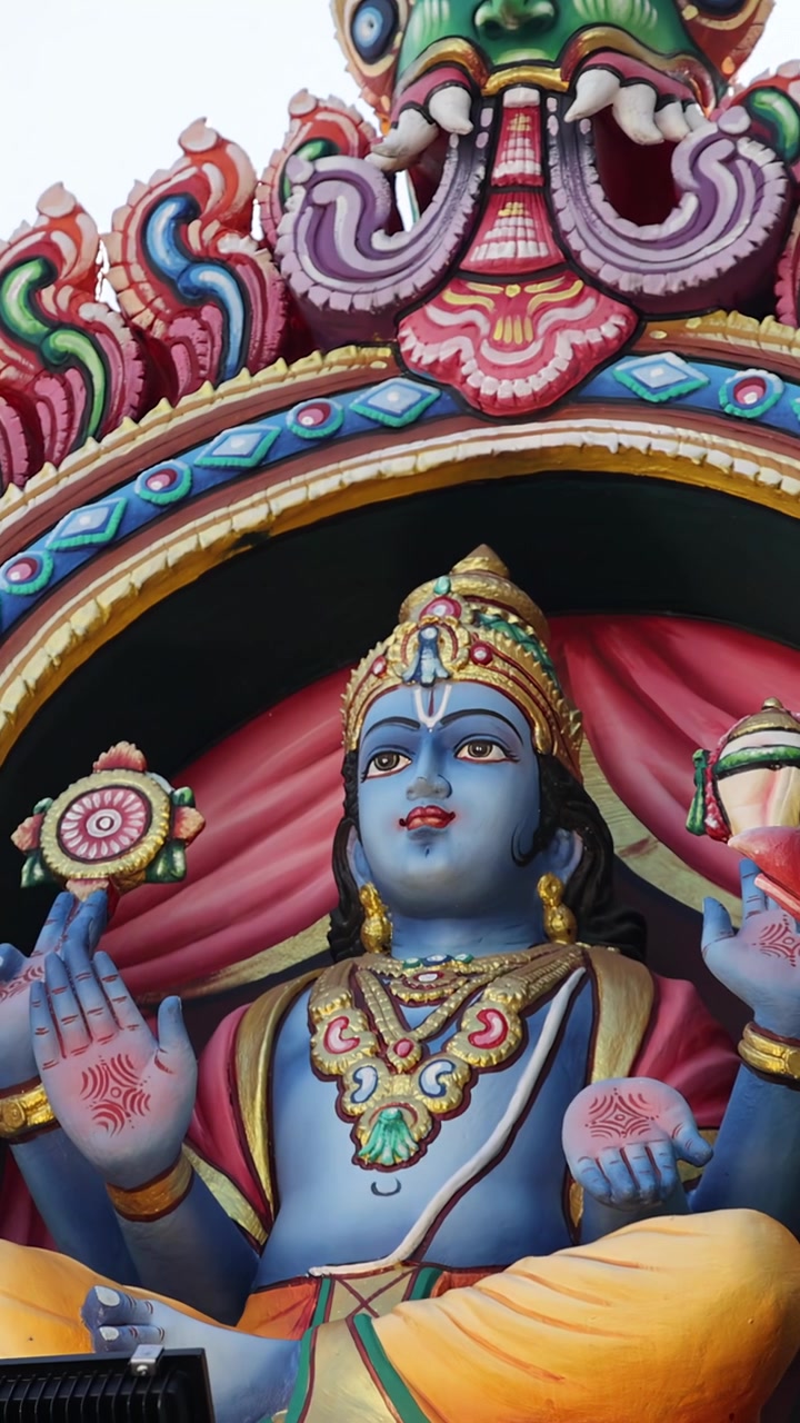 A câmera percorre lentamente estátuas detalhadas e vibrantes na fachada de um templo hindu à luz do dia, destacando o artesanato intrincado, cores vivas e iconografia religiosa
