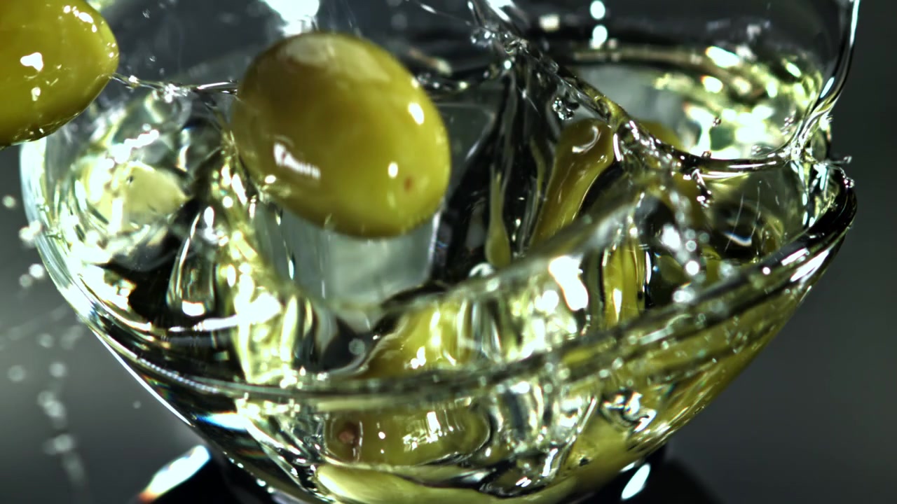 Olive verdi che si tuffano in un liquido trasparente al rallentatore