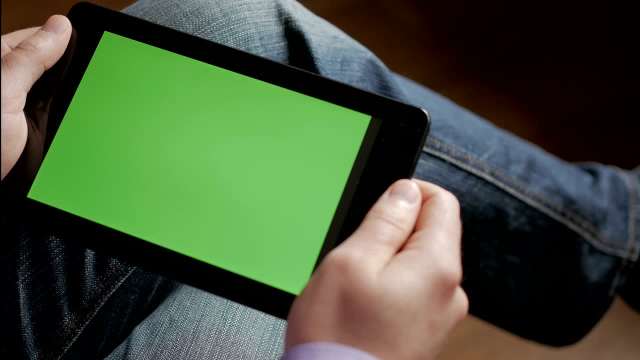 hombre en el lugar de trabajo usando su tableta con pantalla verde, desplazando noticias, comprobando informes financieros, tocando la pantalla. manos vista superior. manos 4k sosteniendo finanzas de negocios teléfono inteligente clave cromo