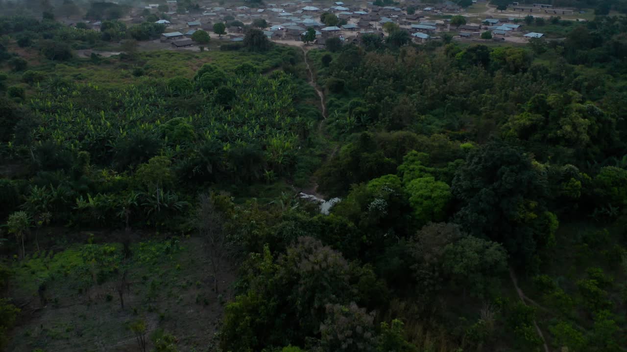 Droneoptagelse, der tilter op af en afrikansk landsby omgivet af skov i Ghana.