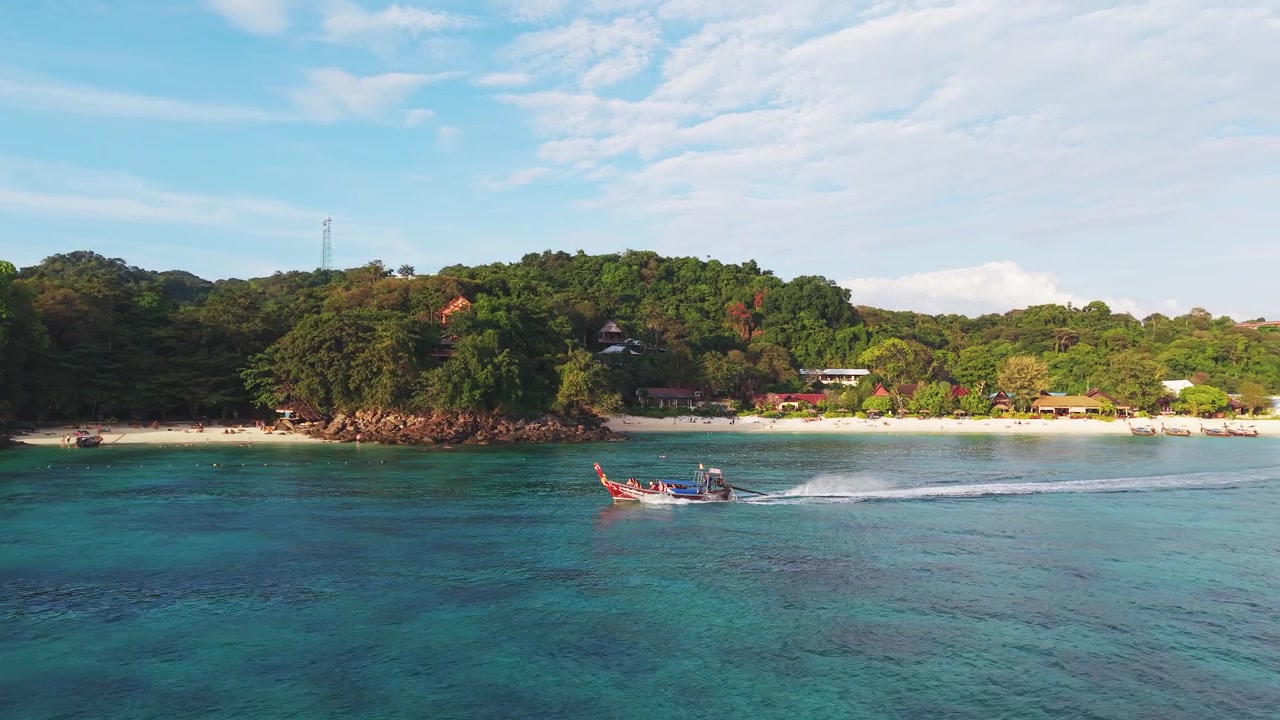 An authentic Thai longtail boat sails through turquoise waters near a lush tropical beach. Perfect for travel documentaries and ecofriendly tourism marketing.