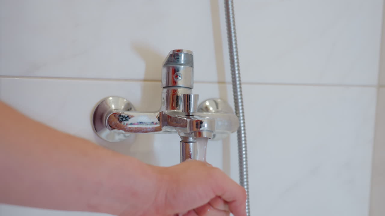 Close up of water running from bathroom tap with hand placed under stream, capturing daily hygiene, household routine, sanitation, and essential use of plumbing fixture for washing