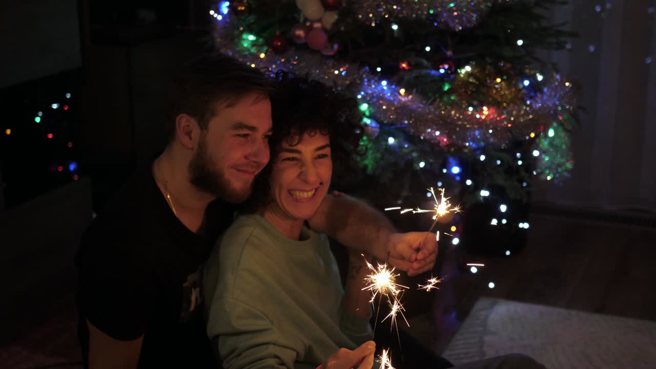 coppia felice innamorata di scintillanti seduta vicino all'albero di natale