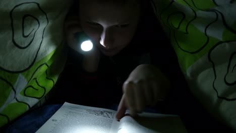 boy reading book in bedroom with flashlight