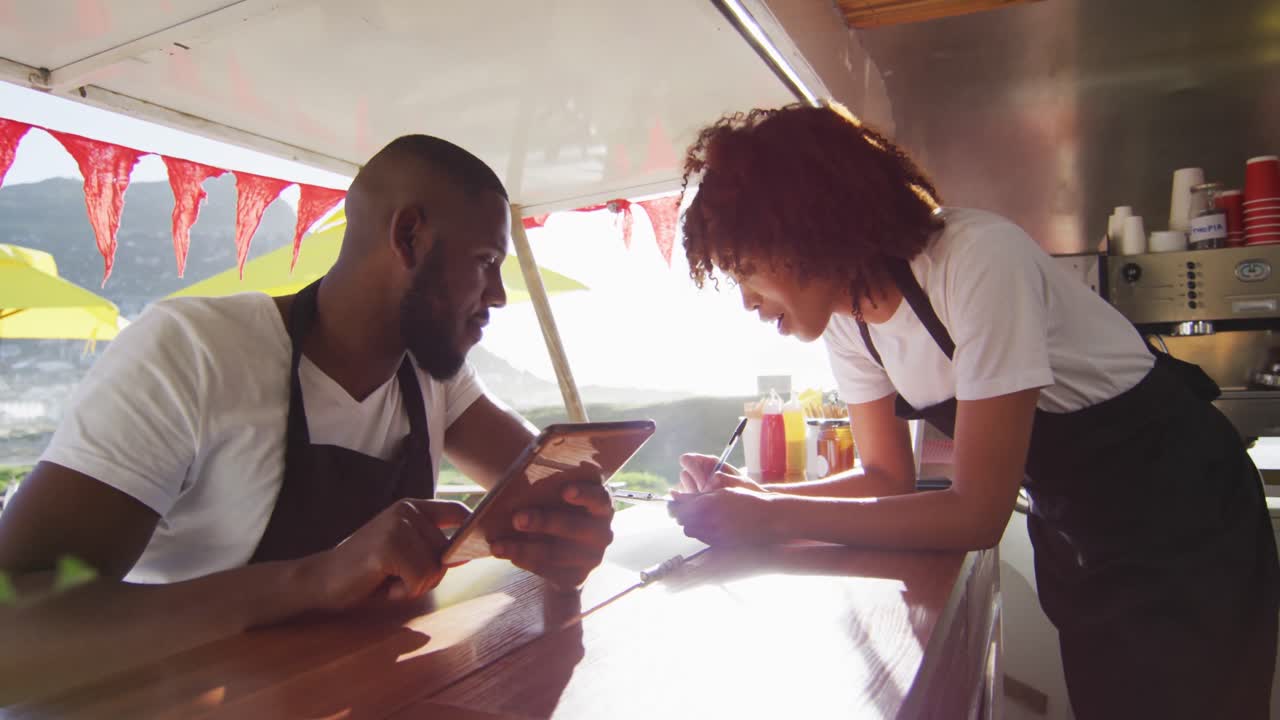 African american couple wearing aprons using digital tablet and taking notes in the food truck