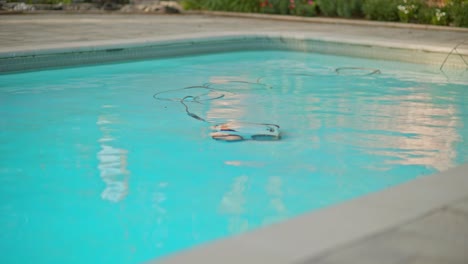 Der-Elektrische-Poolreinigungsroboter-Reinigt-Den-Gesamten-Poolboden,-Wobei-Das-Stromkabel-Im-Klaren,-Reflektierenden-Wasser-Schwimmt