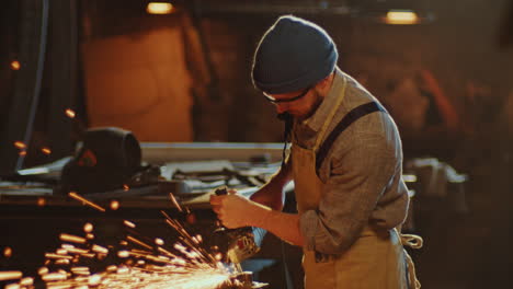 blacksmith working on metal with angle grinder in workshop