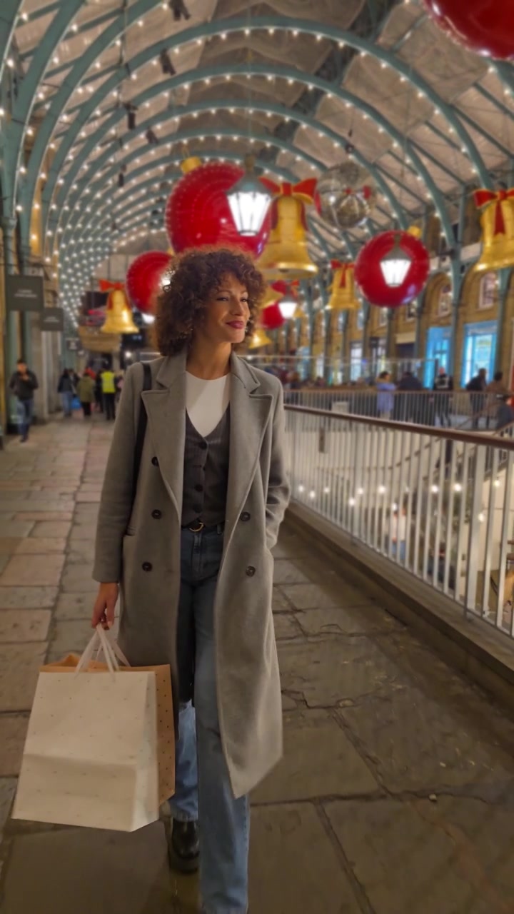 Una donna elegante passeggia tranquillamente attraverso una galleria commerciale adornata con decorazioni festive