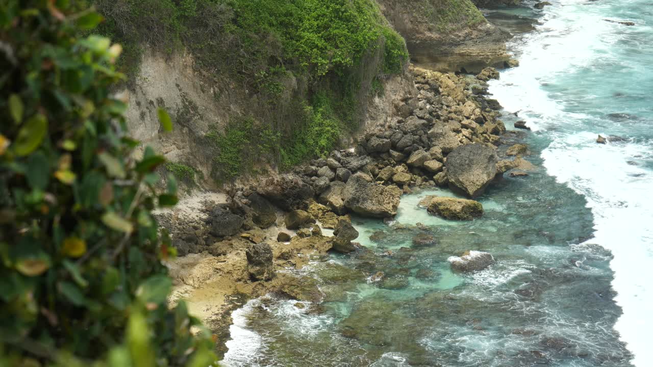 Slow-motion close up of waves breaking on shore below from cliff in Uluwatu, Bali