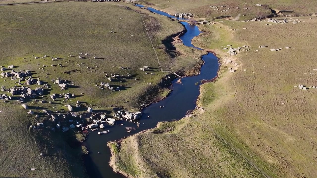 Ripresa aerea con drone dall'alto di un fiume serpeggiante attraverso colline ondulate e pascoli rocciosi a Uralla.