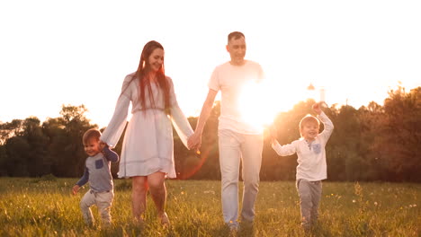 Glückliche-Familie,-Ihr-Mann-Mit-Zwei-Kindern-Geht-Bei-Sonnenuntergang-Im-Abendlicht-Im-Sommer-Bei-Warmem-Wetter-Auf-Dem-Feld-Spazieren.