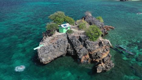 static aerial view of man jumping from platform on rocky islet into turquoise sea, ramblon island archipelago, philippines