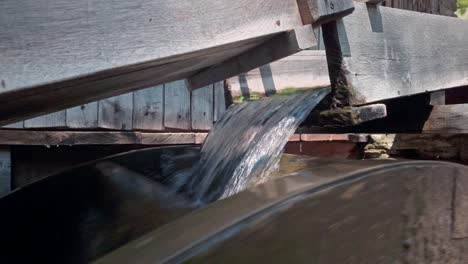 water cascades from sluice flume rotating wooden water wheel