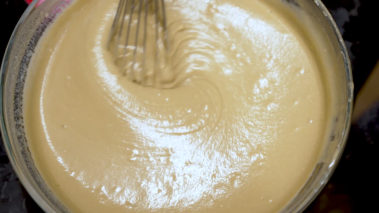 Whisking together smooth cake batter in a glass bowl, achieving the perfect creamy texture essential for delightful baking