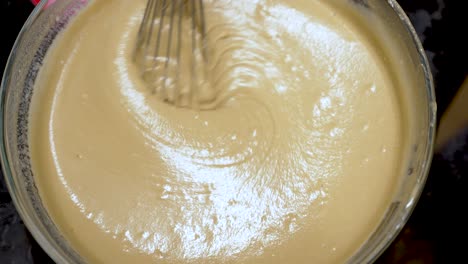 whisking together smooth cake batter in a glass bowl, achieving the perfect creamy texture essential for delightful baking