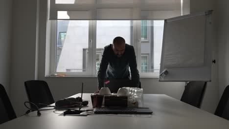 bald male business manager in empty meeting room with arms resting on table shaking head