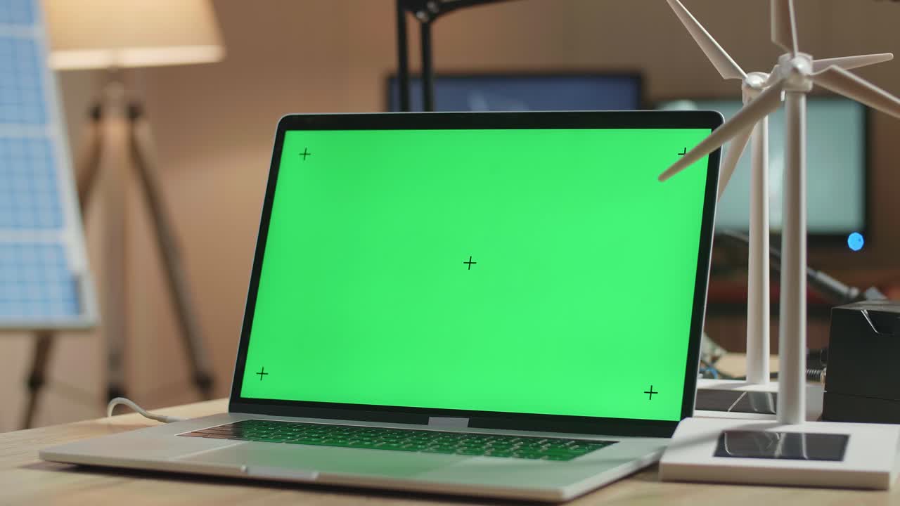 cerca de la pantalla verde de la computadora portátil y la turbina eólica en la mesa al lado de la célula solar en la oficina