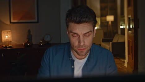 serious employee watching laptop at dark home closeup. exhausted man working