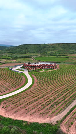 reverse aerial flight revealing a modern winery surrounded by vineyards in la rioja, spain. concept of wine tourism, viticulture, premium wine production and scenic rural architecture