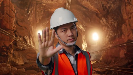 close up of asian male engineer with safety helmet disapproving with no hand sign while standing in underground mine tunnel