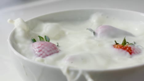 varias fresas cayendo en un tazón de leche a cámara lenta