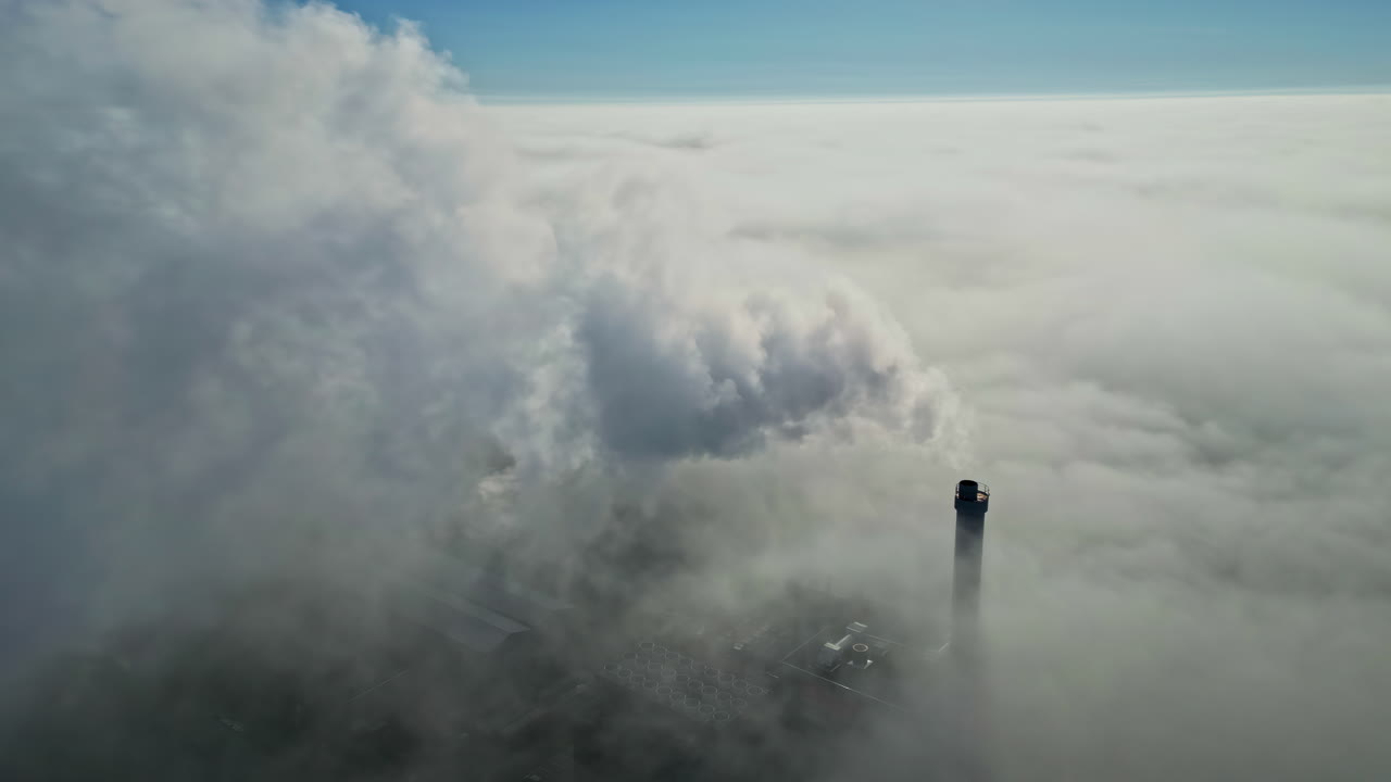 Aerial dolly to smoke rising from industrial tower, white plume above cloudy sky