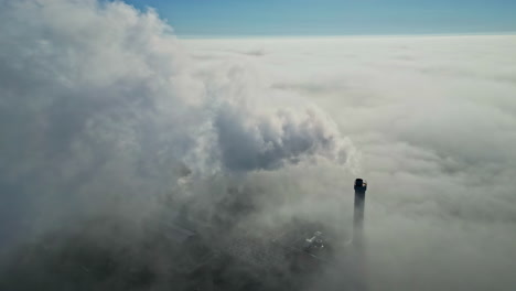 aerial dolly to smoke rising from industrial tower, white plume above cloudy sky