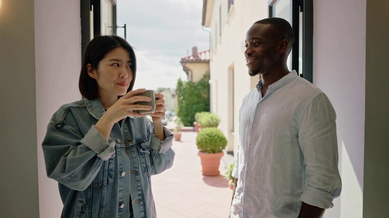 Noticing terrace view man gesturing in doorway while woman in denim jacket lifting mug