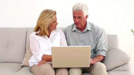 Retired-happy-couple-using-their-laptop-on-the-couch