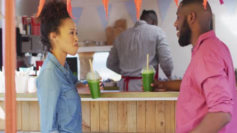 una pareja afroamericana sonriendo mientras beben batidos en el camión de comida