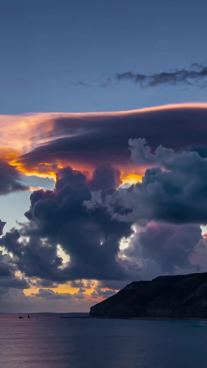Vertical video: Shifting storm cloud showing anvil rim as sun sinking, lighting coastal horizon