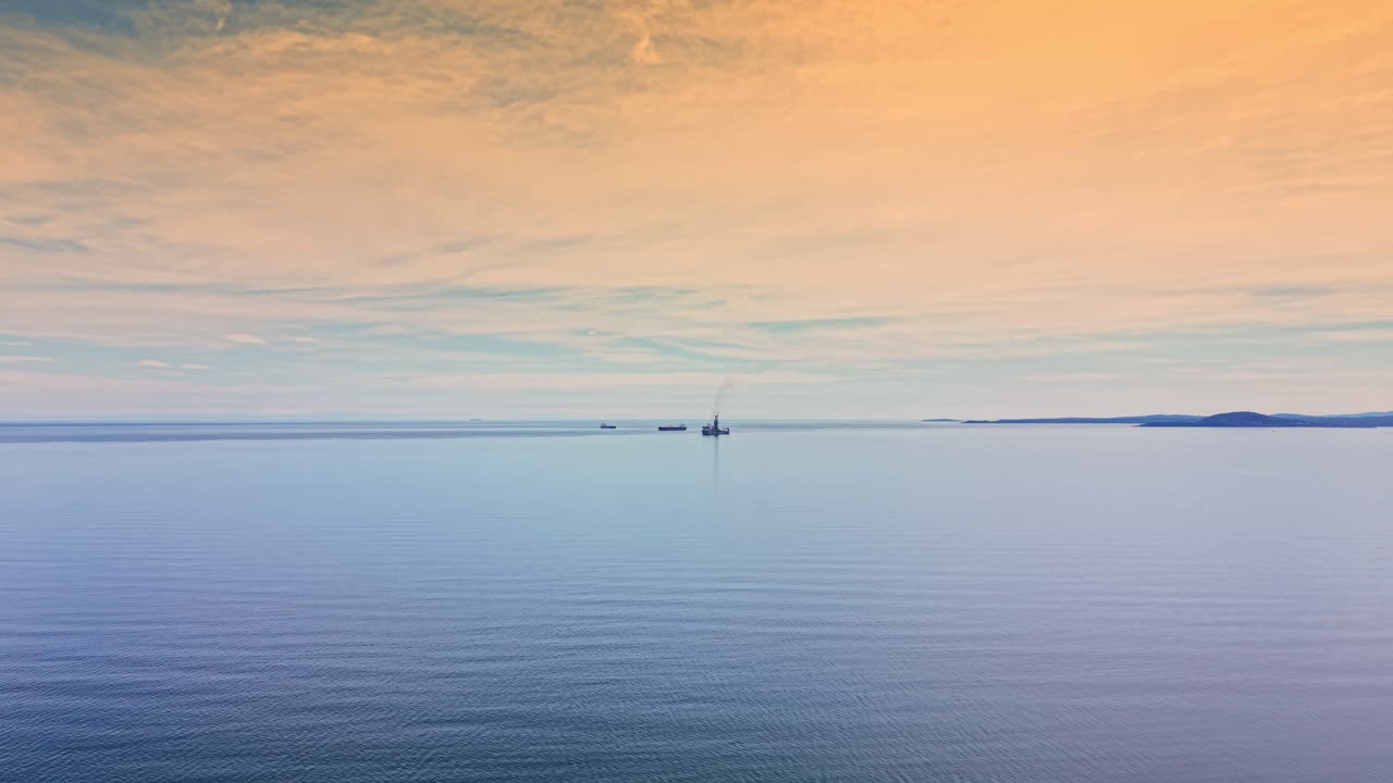 Olietanker navigerer på åbent hav under orange og blå himmel om dagen nær fjerntliggende land