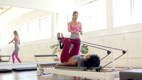 mulher caucasiana guiando mulher biracial em pilates reformador