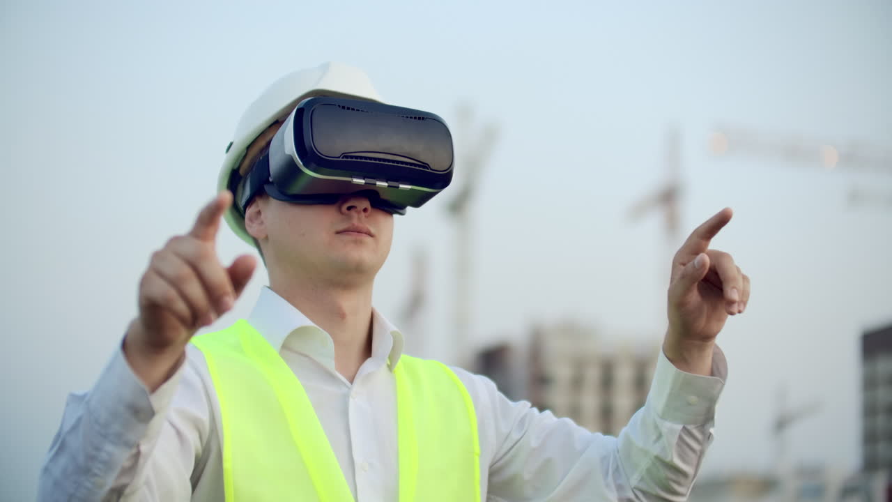 A man in virtual reality glasses helmet and vest on the background of construction controls the hands of the interface and checks the quality of construction and development of the project and the development plan and landscape. Landscape designer uses virtual reality.