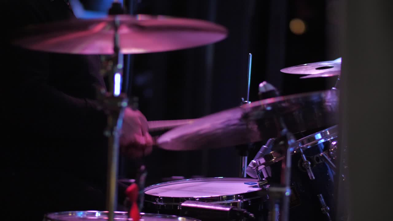 baterista de vista lateral golpeando tambores al ritmo con palos en la fiesta, luces de discoteca interior