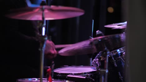 side view drummer hitting drums in rhythm with sticks on party, indoor disco lights