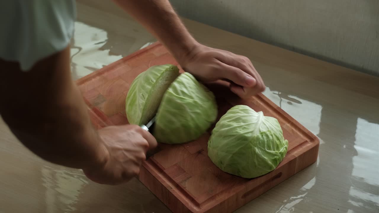 Hands and sharp knife cutting cabbage into quarters for slicing on wooden chopping board.