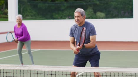 Video-Eines-Glücklichen-Gemischtrassigen-Seniorenpaares-Beim-Training-Auf-Dem-Tennisplatz