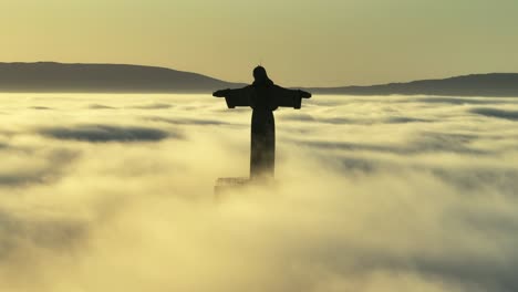 sunrise above the clouds, with birds crossing the horizon by the statue and the fog moving