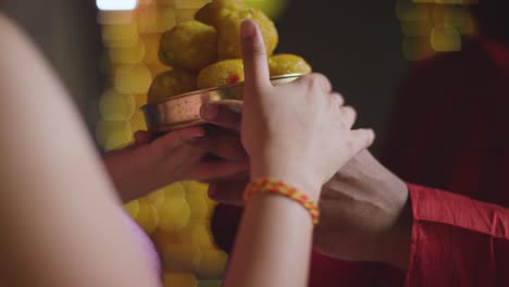 close up of man handing dish of ladoo to woman celebrating festival of diwali