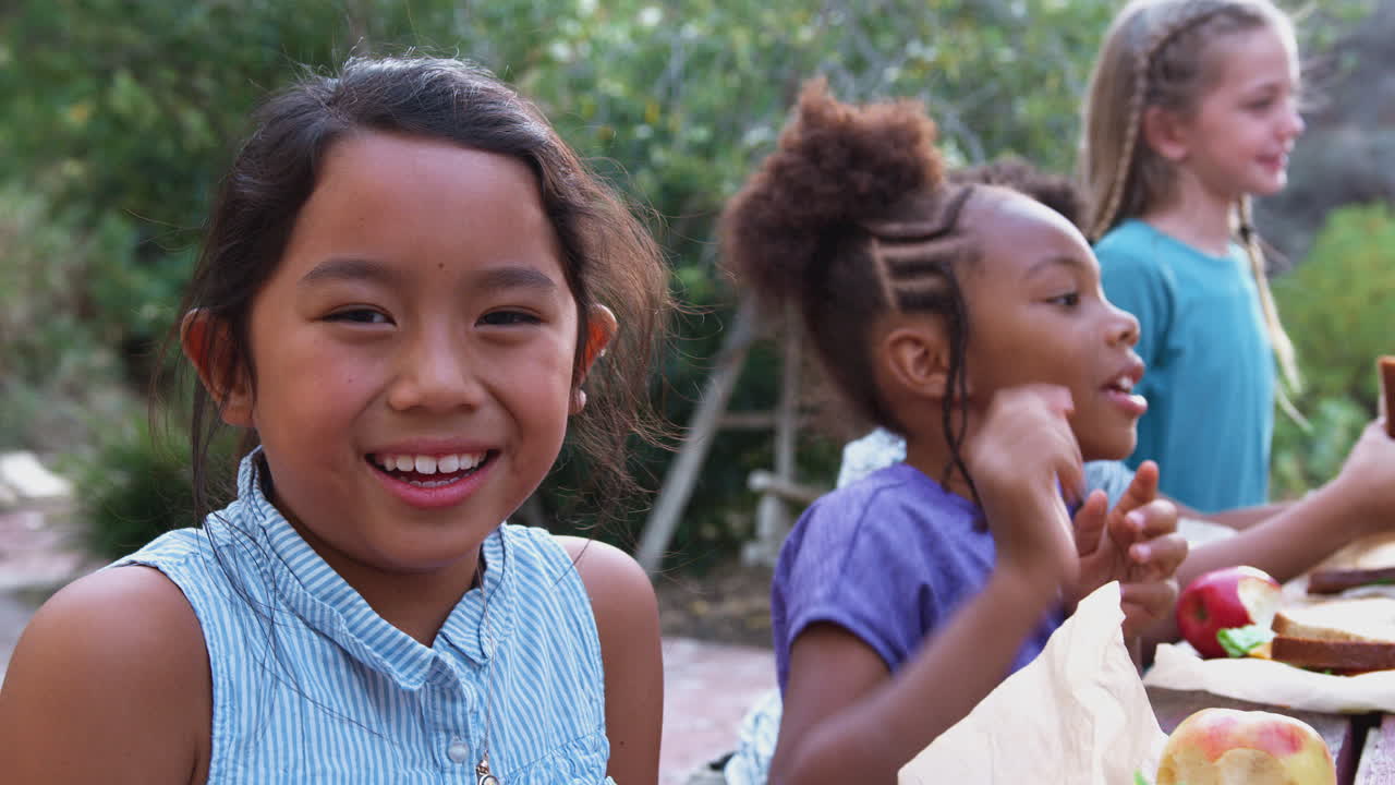 retrato de una niña sonriente con amigos comiendo un picnic saludable en una mesa al aire libre en el campo
