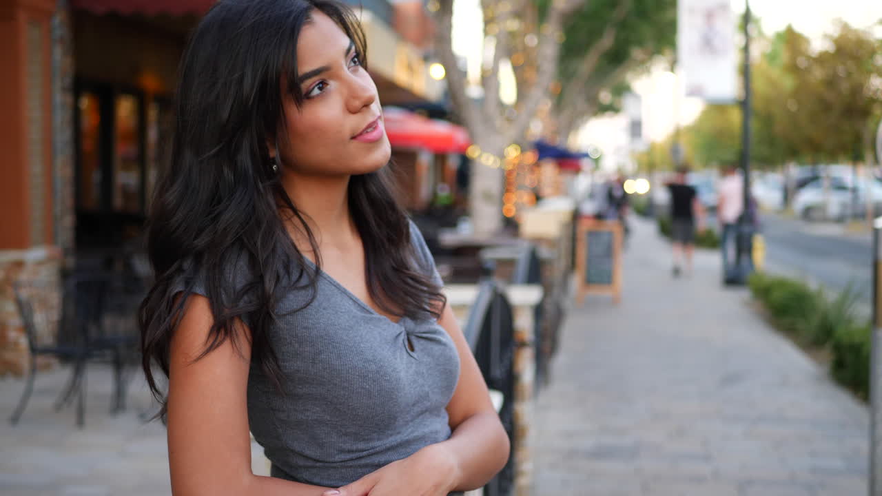 A beautiful hispanic woman with people on a busy downtown urban city street with shops, restaurants and retail stores SLOW MOTION
