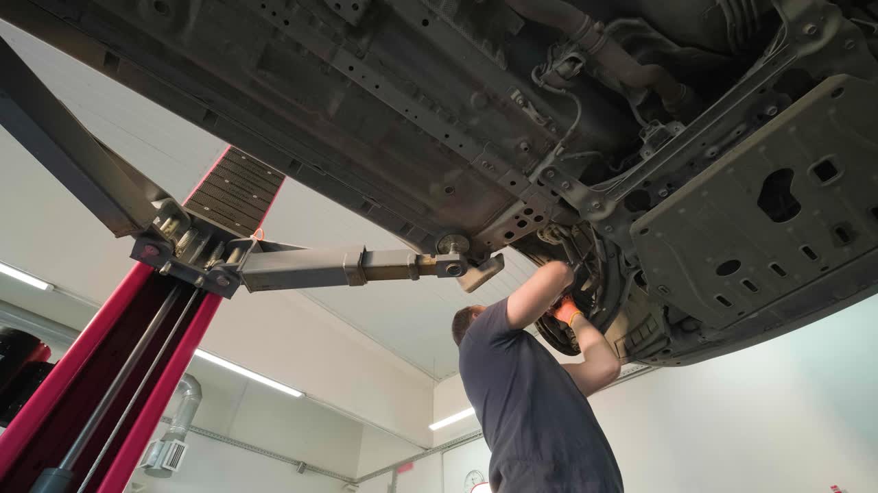 joven mecánico profesional que trabaja bajo el coche moderno levantado en el servicio de reparación de automóviles. servicio de automóviles, mantenimiento de reparación.
