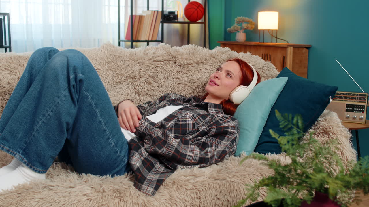 Woman lying on sofa with eyes closed listening to audiobook imagining scenes with peaceful emotion