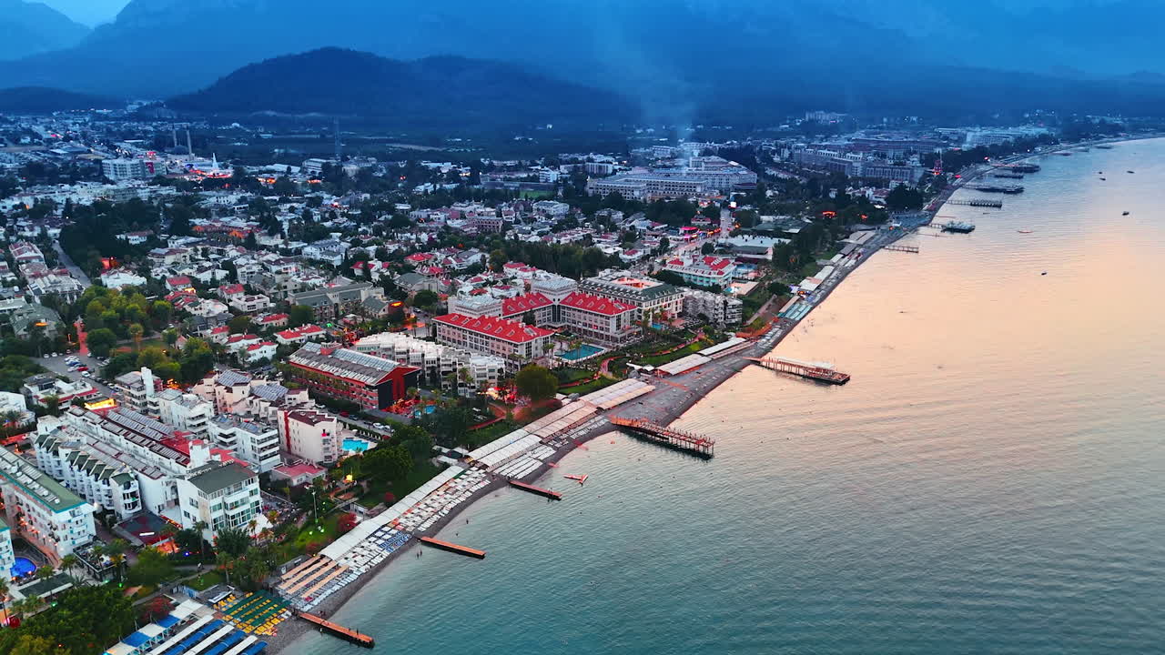 Beautiful resort city of turkey at sunset time. Drone flight over the beaches and yacht club. Mountain silhouettes at backdrop. Kemer, Turkey