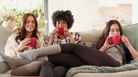 christmas time, women friends relaxing on sofa, enjoying hot drinks together at home