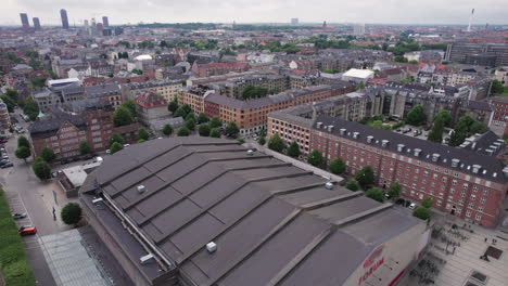 Looking-down-from-above,-you'll-see-the-Forum-building-immersed-in-the-vibrant-city-atmosphere,-encircled-by-buildings-and-cars