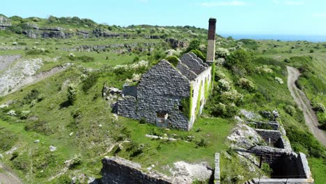 abandoned overgrown ivy covered desolate countryside historical welsh coastal brick factory mill aerial view slow right orbit to front