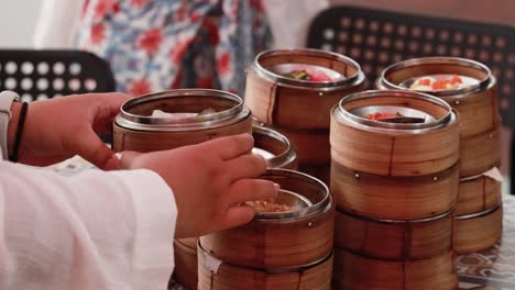 hands selecting dim sum from bamboo steamers on a table in a relaxed dining setting
