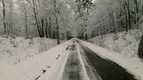 Low-angle-drone-flying-forward-along-the-snow-covered-and-ice-covered-countryside-forest-road,-huge-snowdrifts-on-sides-daytime